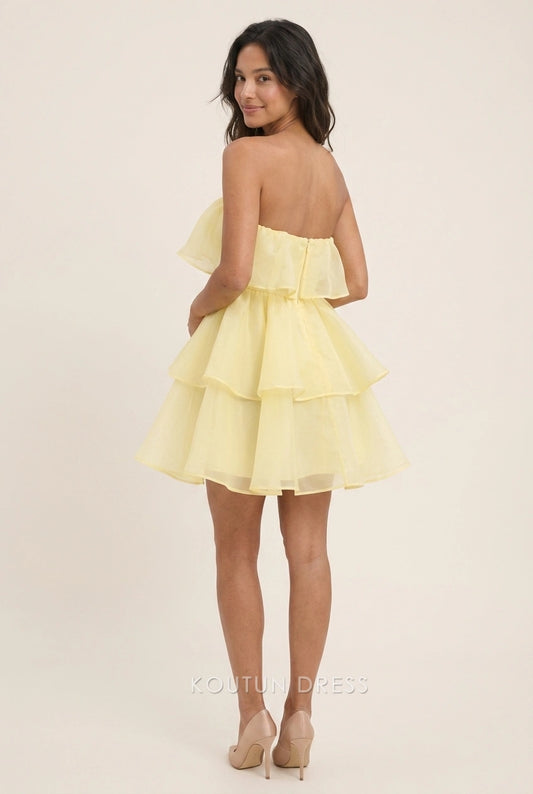 Model posing in a pale yellow tiered strapless mini dress for homecoming.