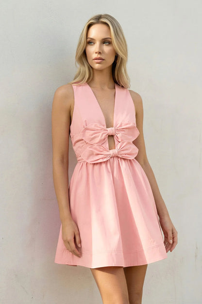 Model wearing a blush pink A-line mini homecoming dress with V-neck and double bow details.