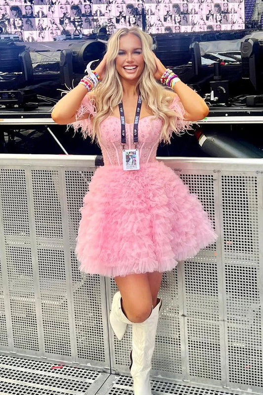 Model wearing a pink A-line off-shoulder homecoming dress with feather trim.