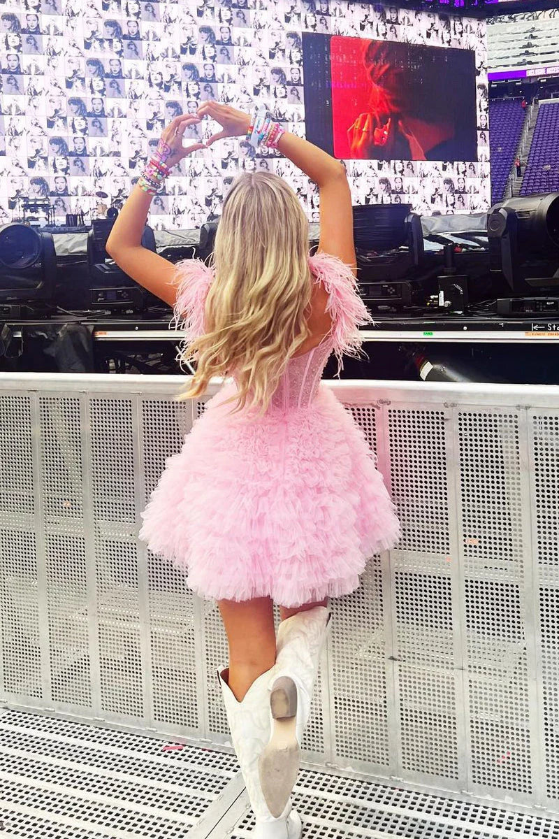 Side view of a model in a pink A-line off-shoulder dress with feather accents.