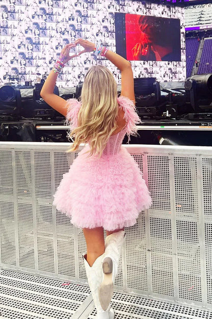 Side view of a model in a pink A-line off-shoulder dress with feather accents.