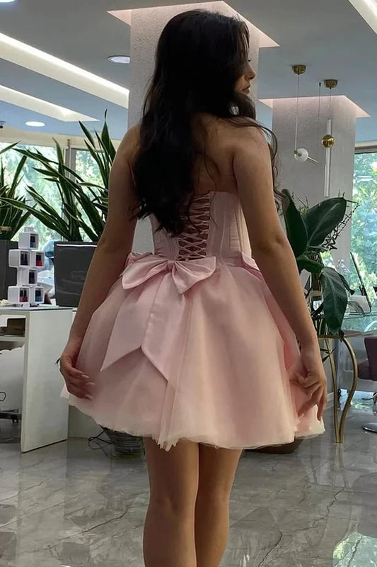 Back view of pink A-line strapless dress showing lace-up corset and bow detail.