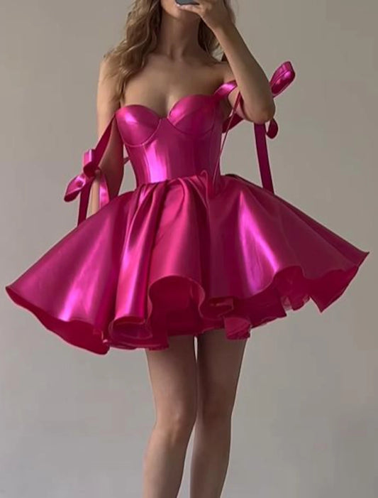 Pink A-line satin homecoming dress with spaghetti straps and bow detail.