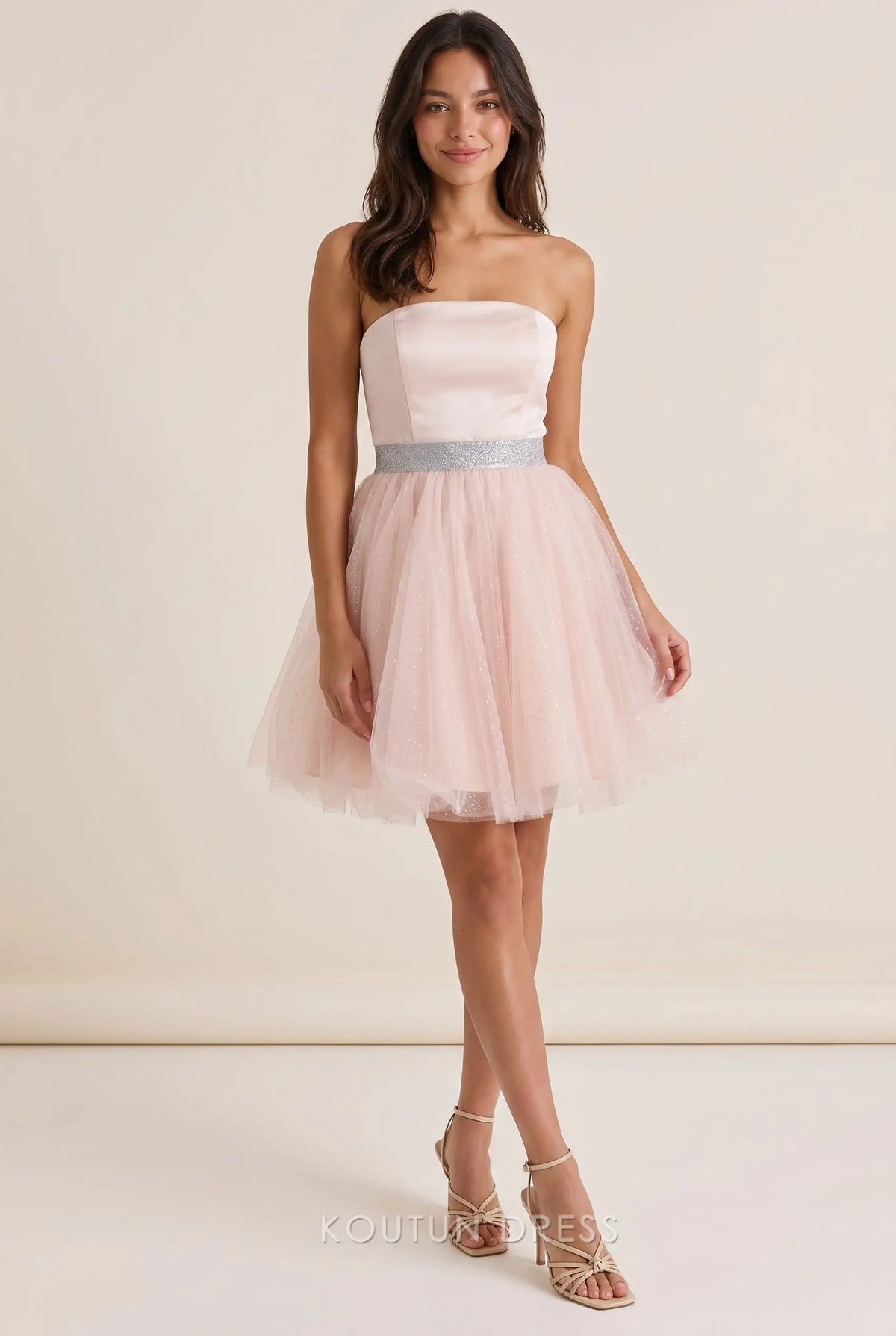 Model wearing a blush pink strapless A-line mini homecoming dress with a silver rhinestone waistband.