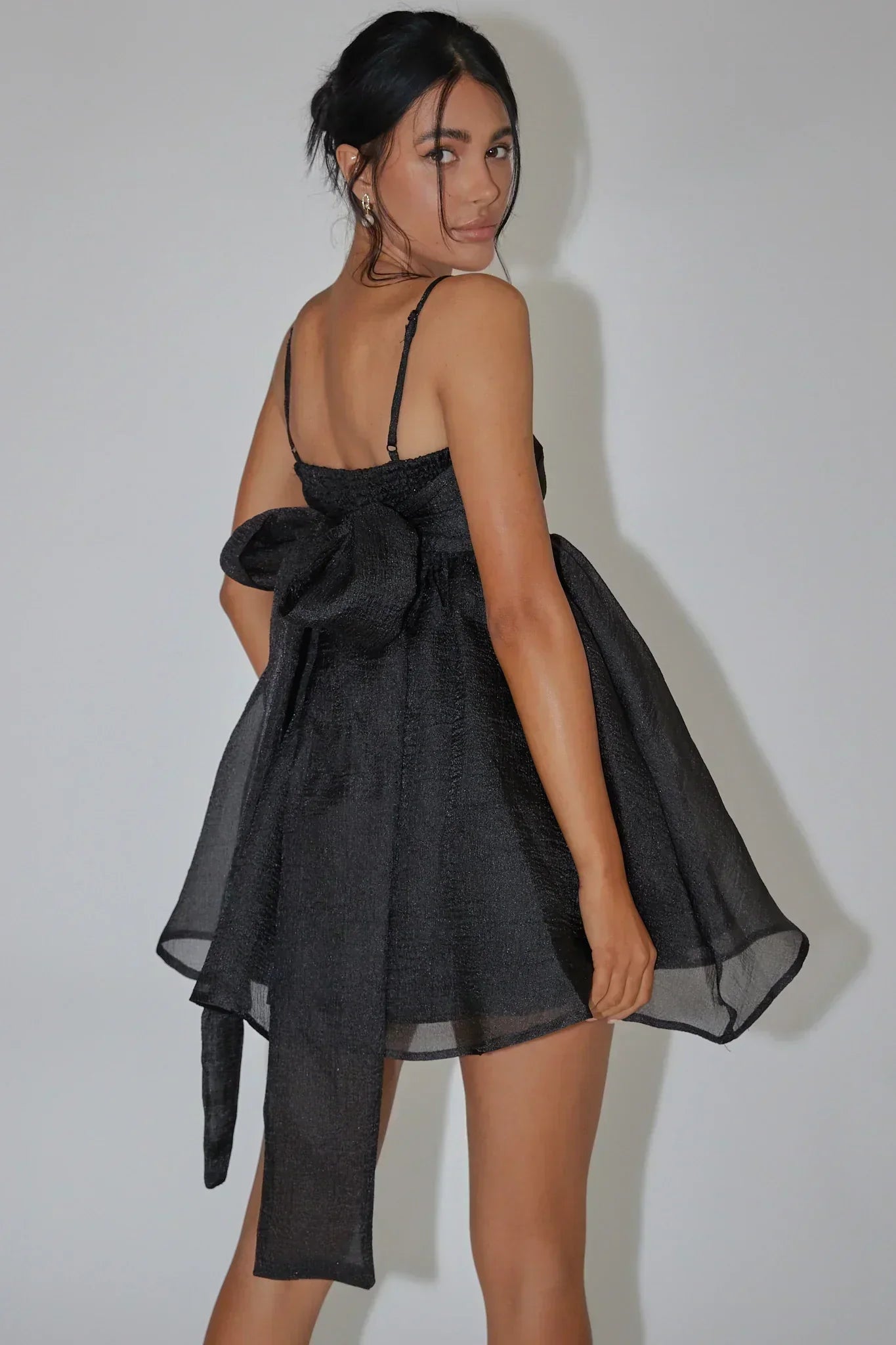 Back view of a model in a black babydoll dress, highlighting the oversized bow.