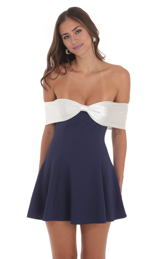 Model wearing a navy satin off-shoulder homecoming dress with a front bow.