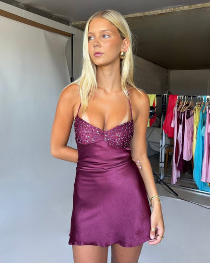 Model wearing a purple sheath homecoming dress with spaghetti straps and beading.