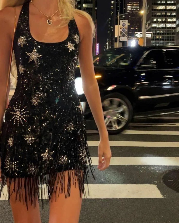 Model wearing a black sequin halter homecoming dress with starburst beading and fringe hem.