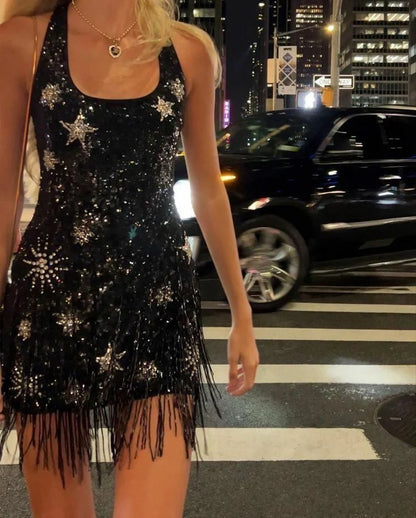 Model wearing a black sequin halter homecoming dress with starburst beading and fringe hem.
