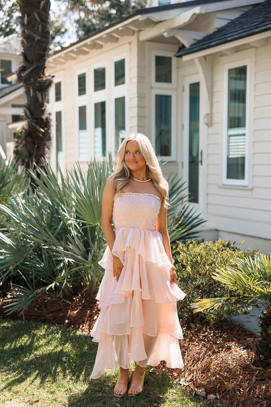 Model wearing a soft pink strapless tiered ruffle chiffon maxi prom dress with a smocked bodice.