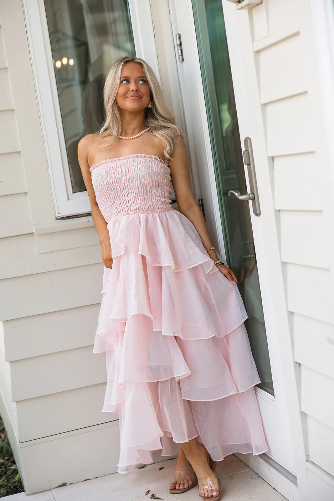 Model posing in a soft pink strapless tiered ruffle prom dress, showing the full length.