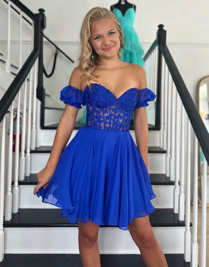 Model wearing a royal blue A-line off-shoulder homecoming dress with lace appliques.