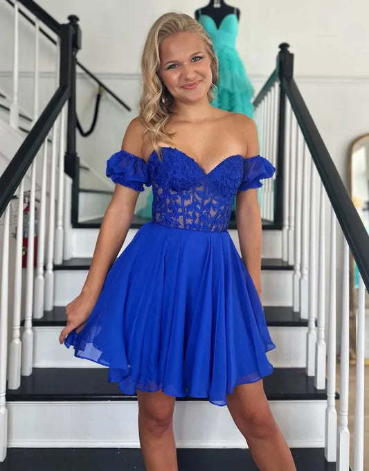Model wearing a royal blue A-line off-shoulder homecoming dress with lace appliques.