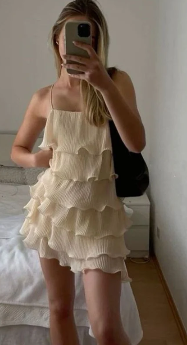 Woman wearing an elegant ruffled pleated mini homecoming dress with spaghetti straps.