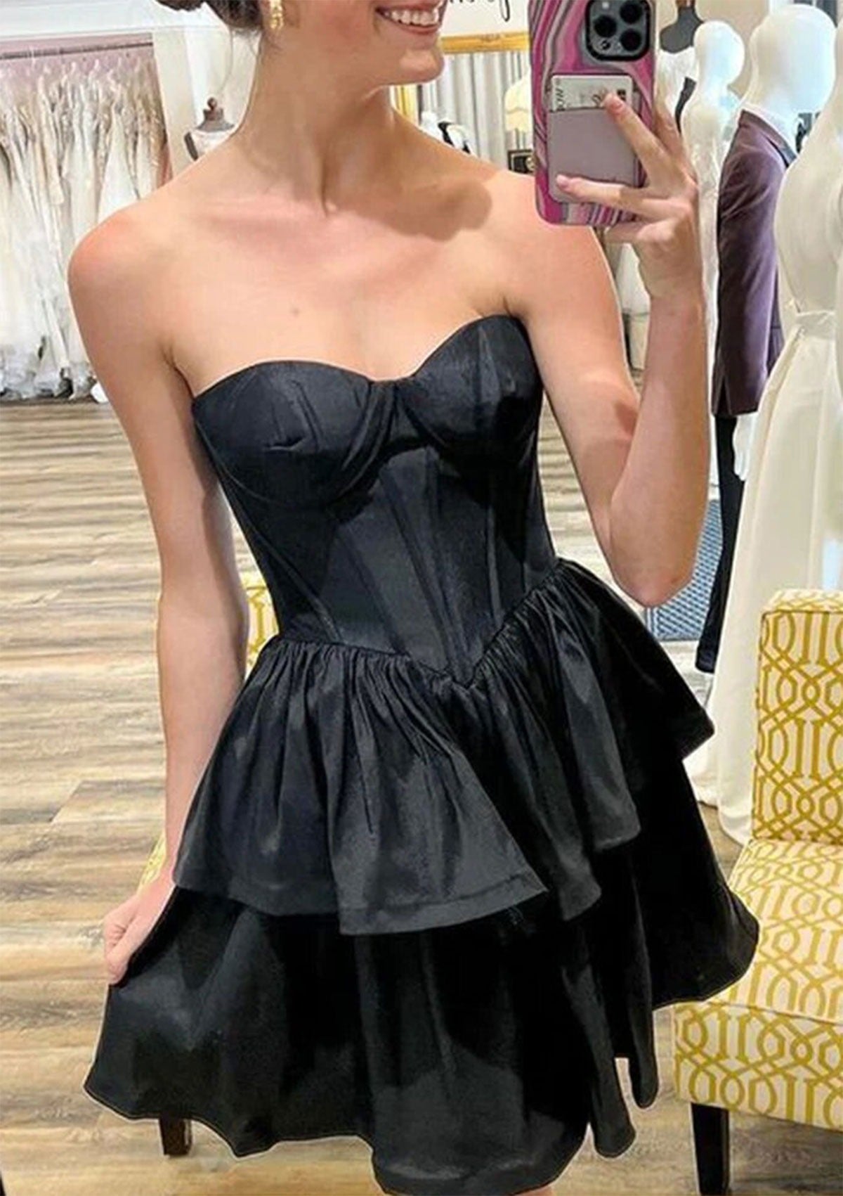 Model wearing a black strapless sweetheart corset tiered satin A-line short homecoming dress.