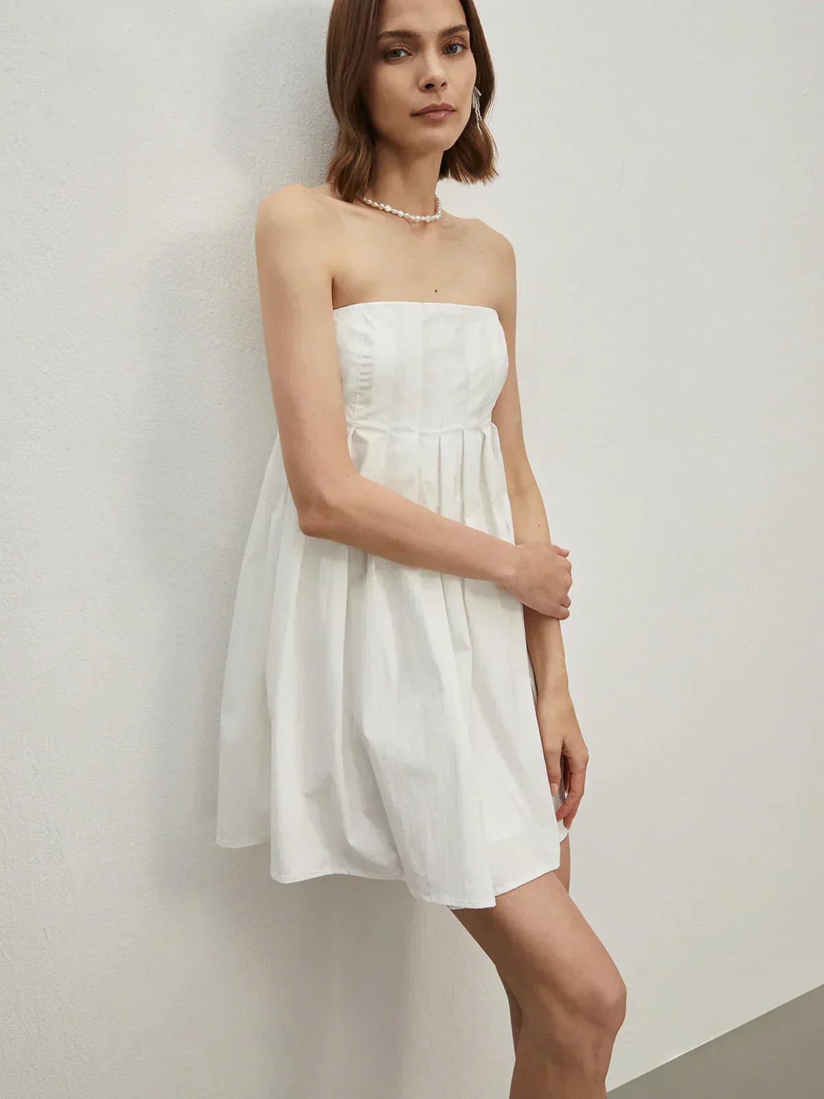 Side profile of white cotton blend pleated mini dress.