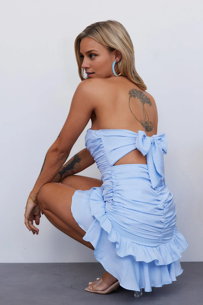Side view of a model in a blue strapless ruched bodycon mini dress.