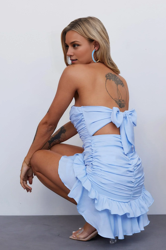 Side view of a model in a blue strapless ruched bodycon mini dress.