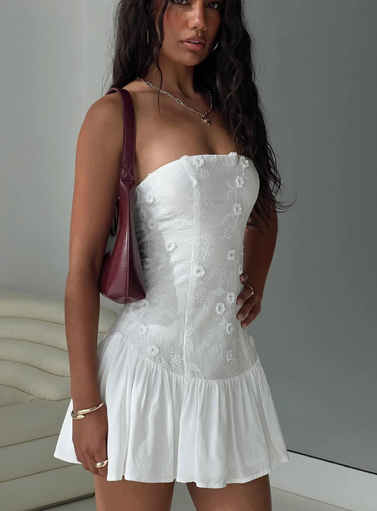 Model wearing a white strapless mini homecoming dress with floral appliques and ruffled hem.