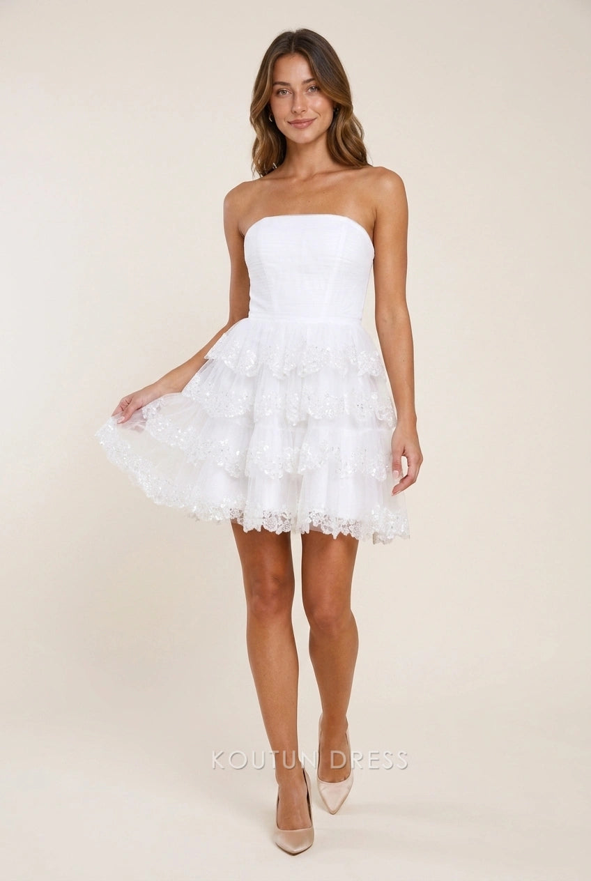 Model wearing Koutun elegant white sequin strapless tiered short homecoming dress.
