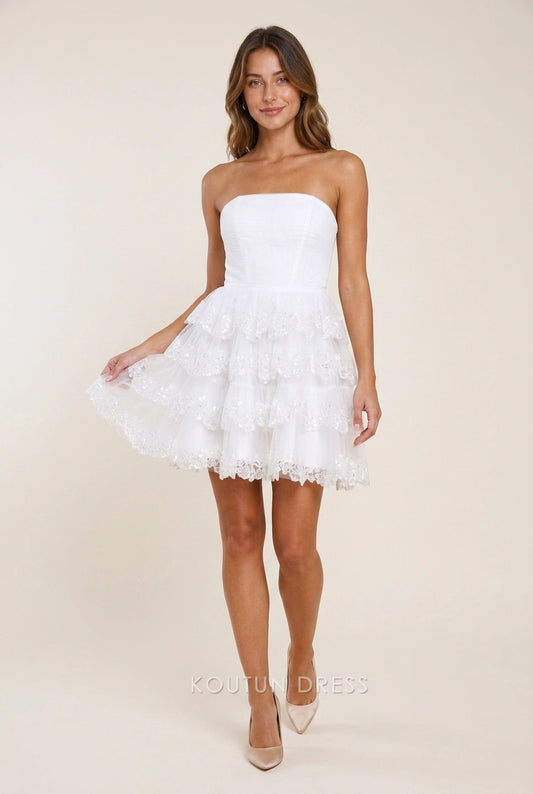 Model wearing Koutun elegant white sequin strapless tiered short homecoming dress.