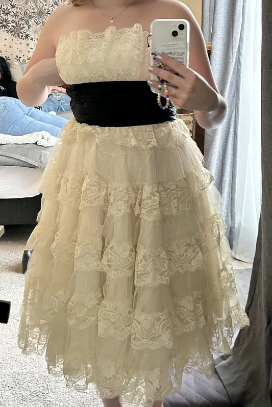 Vintage-inspired A-line strapless midi homecoming dress with tiered lace and tulle, featuring a contrast waist sash.