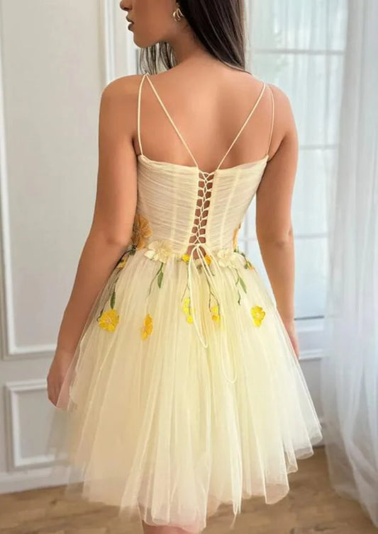 Back view of a yellow short homecoming dress featuring floral details and a ruffled skirt.