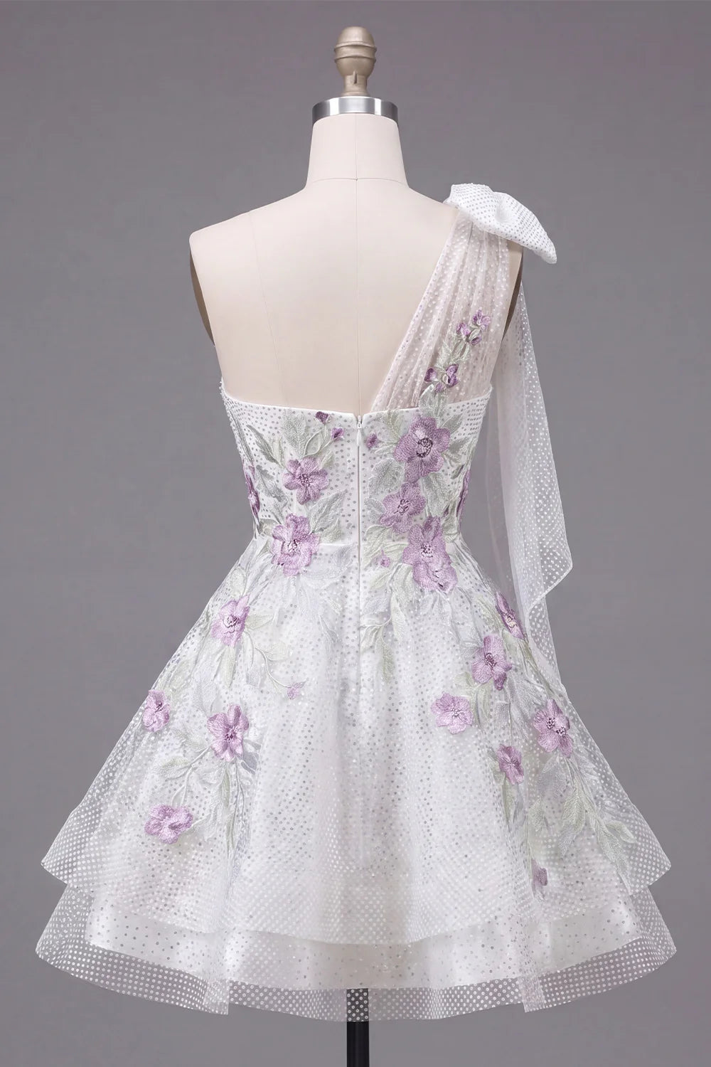 Detail of the large sheer bow on the one-shoulder neckline of the white dress.