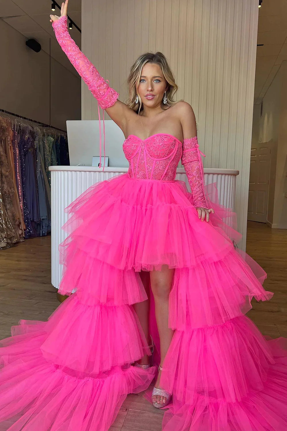 Model wearing a hot pink high-low corset homecoming dress with detachable lace sleeves.
