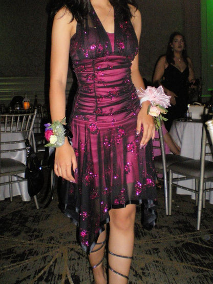 Model wearing a black and magenta glitter floral short homecoming dress with a halter neck and ruched mesh bodice.