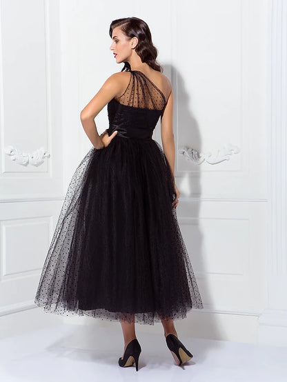 Side profile of a model in a black one-shoulder A-line tulle dress, showcasing the silhouette.