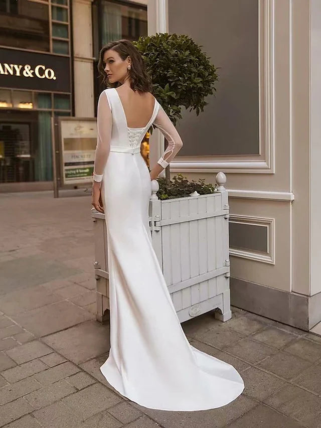 Side profile of a bride in a white satin mermaid trumpet wedding dress, showing the fitted bodice and flowing skirt.